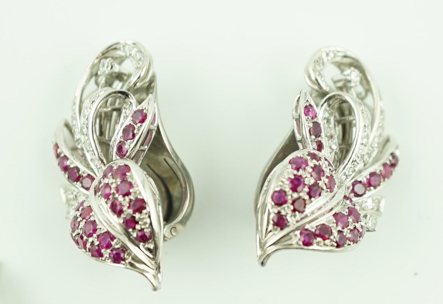 A suite of platinum?, diamond and ruby set cluster jewellery, comprising a spray brooch and pair of matching ear clips